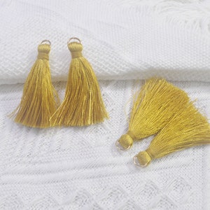 Puede incluir: Cuatro borlas doradas con un lazo en la parte superior. Las borlas están hechas de hilos finos y suaves y son perfectas para agregar un toque de elegancia a cualquier proyecto.