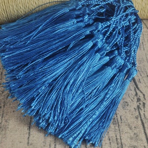 May include: A bundle of bright blue tassels. Each tassel is made of many strands of shiny, silky material, tied together at the top. The tassels are a vibrant, solid blue color, and are likely used for crafting or decorative purposes.