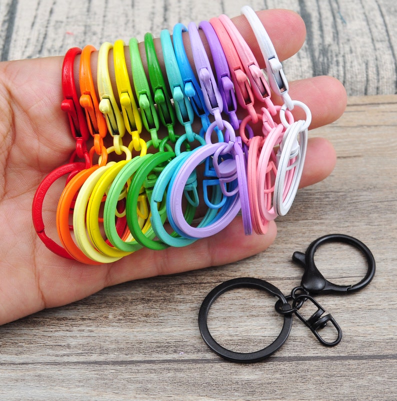 Puede incluir: Un juego de llaveros de metal de colores en un arco&iacute;ris de colores, incluyendo rojo, naranja, amarillo, verde, azul, morado y blanco. Los llaveros est&aacute;n todos conectados entre s&iacute; y se sostienen en una mano. Tambi&eacute;n hay un solo llavero de metal negro con un cierre giratorio.