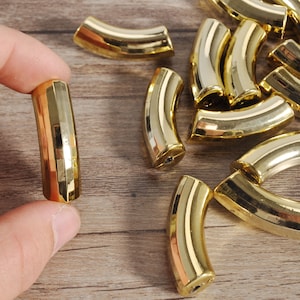 May include: A close-up of a collection of gold-colored metal half-round shapes. The shapes are arranged in a random pattern on a wooden surface. One shape is being held by a hand.