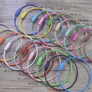 May include: A selection of coloured cable keyrings with a metal ring and a plastic cap on one end. The keyrings are laid out in a row on a wooden surface. The colours include light purple, light yellow, blue, yellow, light blue, pink, green, khaki, aqua, rose, brown, orange, white, light grey, red, light pink, light green, black, and sky blue.