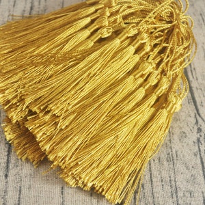 May include: A bundle of gold tassel trim, made of thin, silky threads. The tassels are tied together at the top, creating a uniform and elegant look.