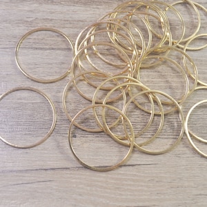 May include: A selection of gold-coloured metal rings, spread across a light brown wooden surface. The rings are thin and circular, with a slightly textured appearance. The lighting highlights the metallic sheen of the rings, creating a warm, inviting aesthetic.
