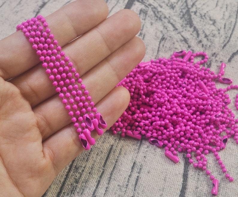 May include: A close-up of a pile of bright pink metal chain, with a few strands held in a hand. The chain is made of small, round links.
