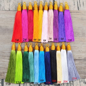 Könnte beinhalten: Einundzwanzig bunte Quasten mit goldenen Spitzen. Die Quasten sind in zwei Reihen auf einer Holzoberfläche angeordnet. Die Quasten sind von 1 bis 21 nummeriert.