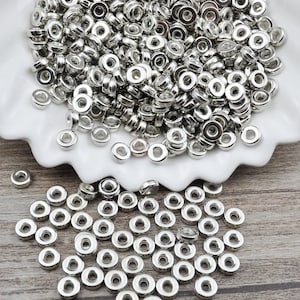 May include: A large pile of silver metal spacer beads, some of the beads are scattered on a wooden surface.