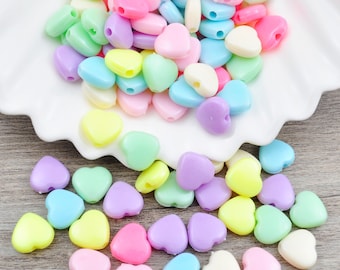 May include: Assortment of pastel colored heart shaped plastic beads. The beads are in a variety of colors including pink, blue, yellow, green, and purple.