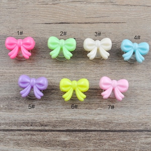 以下が含まれることがあります： 7つのカラフルなプラスチック製の蝶ネクタイ型のボタン。各ボタンの下に1から7までの数字が印刷されています。