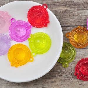 Puede incluir: Surtido de abalorios de sombrero de plástico de colores con un detalle de lazo. Los abalorios son de varios colores, incluyendo rojo, rosa, morado, amarillo, verde y naranja.