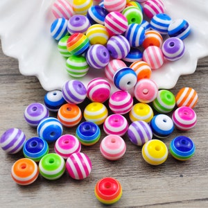Puede incluir: Una colección de cuentas rayadas de colores. Las cuentas son de plástico y tienen un acabado brillante. Son perfectas para hacer joyas u otras manualidades.