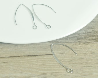 May include: Two pairs of silver-toned earring hooks, each with a loop at the top. The hooks are on a white plate and a wooden surface.