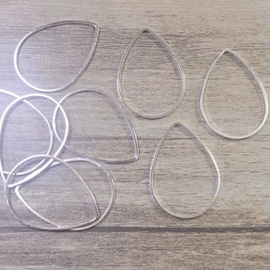 May include: A set of six silver teardrop-shaped metal hoops. The hoops are arranged on a wooden surface.