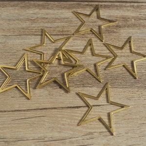 May include: A set of eight gold-colored metal star shapes, arranged in a cluster on a wood surface.