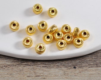 May include: A collection of gold-colored metal beads with a decorative, textured design. The beads are round with a hole in the center.