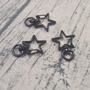 Puede incluir: Tres cierres giratorios negros en forma de estrella con un anillo circular y una puerta con resorte. Los cierres son de metal y están diseñados para sujetarse a llaveros, cordones u otros accesorios. Los cierres se muestran sobre una superficie gris claro.
