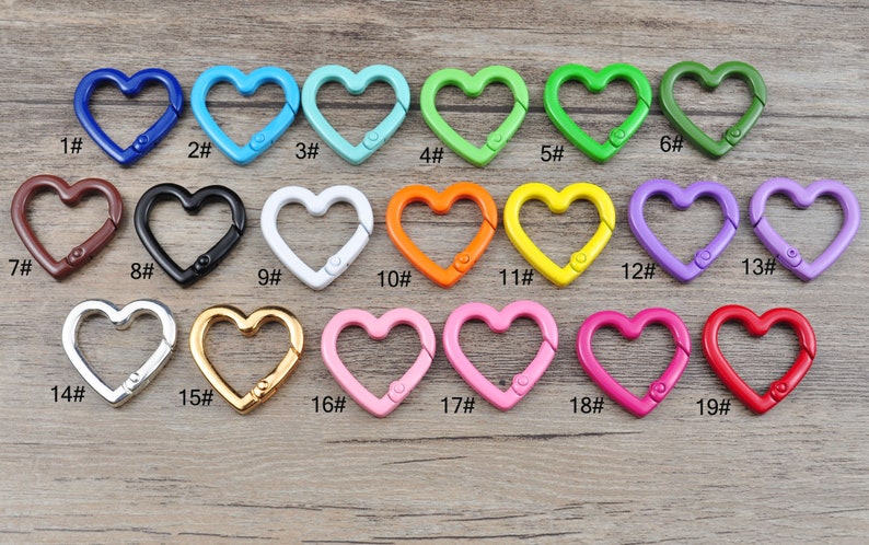 May include: A collection of heart-shaped carabiner clips in various colors, including blue, green, pink, and red. Each clip has a metal clasp and is numbered from 1 to 19. These decorative clips are suitable for attaching to keychains or bags.