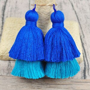 May include: A pair of blue and turquoise tassel earrings. The earrings are made of two layers of tassels, with the top layer being blue and the bottom layer being turquoise.