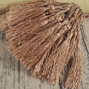 Könnte beinhalten: Ein Bündel brauner Quastenbesatz mit einem Knoten oben. Die Quasten sind aus weichem, seidenartigem Material und etwa 5 cm lang.