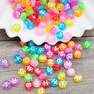 May include: Assortment of colorful plastic alphabet letter beads. The beads are round and have a white letter on each side. The letters are A, B, C, D, E, F, G, H, I, J, K, L, M, N, O, P, Q, R, S, T, U, V, W, X, Y, and Z.