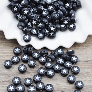 May include: Black and white star-shaped beads. The beads are round and have a white star design on a black background.