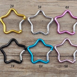 Op de afbeelding: Tien stervormige metalen sleutelhangers in verschillende kleuren, genummerd van 1 tot en met 10. De sleutelhangers zijn gerangschikt in twee rijen van vijf.