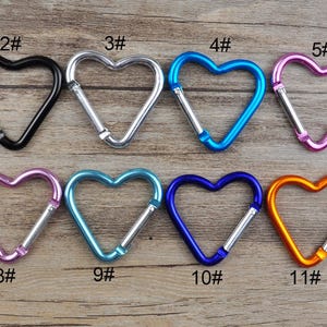 May include: Twelve heart-shaped metal keychains in various colors, including red, black, silver, blue, pink, purple, green, and orange. Each keychain is numbered 1 through 12.