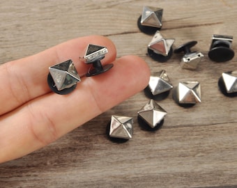 May include: Silver-colored, geometric studs with a pyramid design. The studs are on black bases, and several are scattered on a wooden surface. The studs are small, with a shiny, metallic finish, and are suitable for various craft projects.