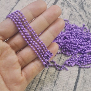 May include: A close-up of a hand holding multiple strands of lavender colored metal chain. The chain is made of small, round links.