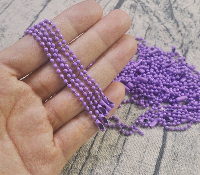 May include: A close-up of a hand holding multiple strands of lavender colored metal chain. The chain is made of small, round links.