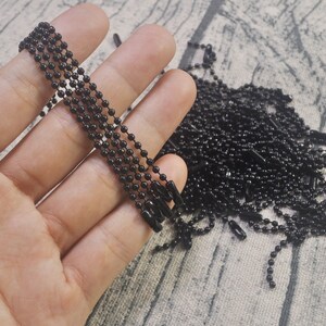 May include: A close-up of a hand holding a bundle of black metal chains. The chains are made of small, round links and are perfect for crafting jewelry or other projects.