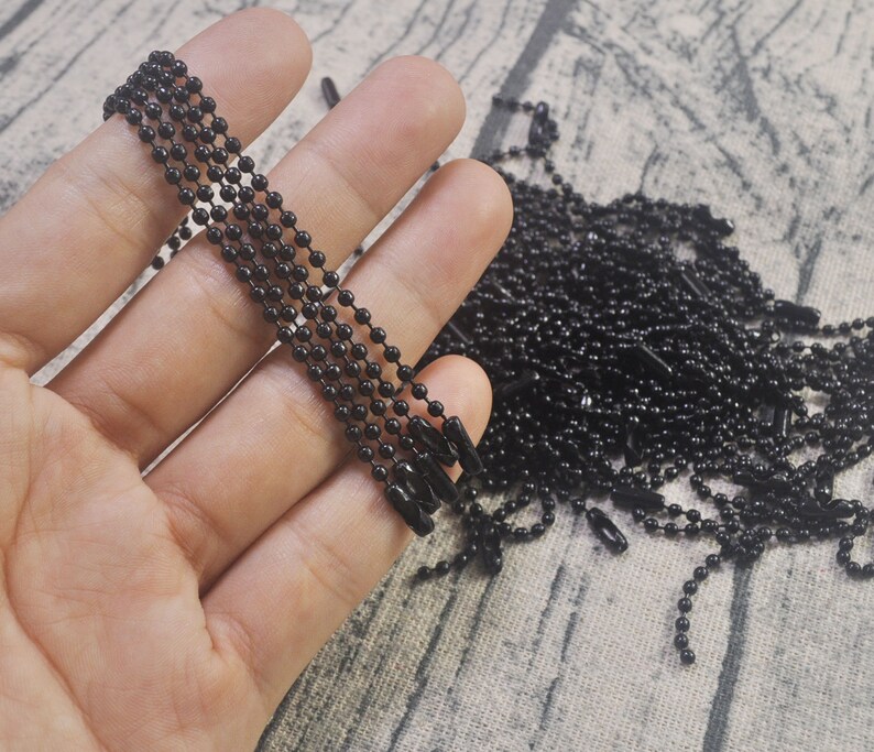 May include: A close-up of a hand holding a bundle of black metal chains. The chains are made of small, round links and are perfect for crafting jewelry or other projects.