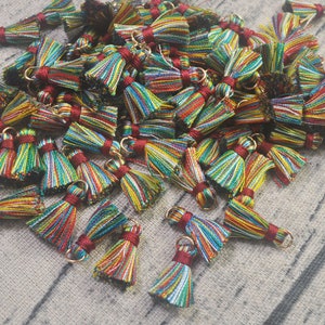 Puede incluir: Un montón grande de borlas multicolores a rayas con anillos de metal dorado. Las borlas están hechas de hilo y miden aproximadamente 2,5 cm de largo.
