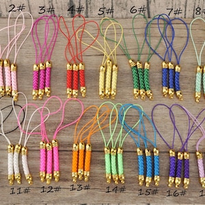 May include: A collection of 18 decorative tassels in various colors, including brown, pink, red, yellow, green, blue, and purple. Each tassel features a braided design with gold-colored metal accents and a loop for hanging.