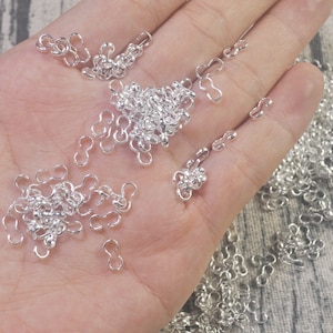May include: A close-up of a hand holding a large quantity of silver-toned metal jump rings. The jump rings are small and have a simple, classic design.