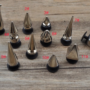 Peut inclure: Onze clous en métal argenté en forme de pyramide et de cône avec des bases noires. Les clous sont numérotés de 1 à 11.