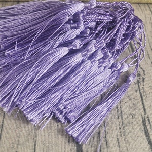 Può includere: Un gruppo di nappe di colore lavanda con fili lunghi. Le nappe sono realizzate in un materiale morbido e setoso e hanno un aspetto delicato ed elegante.