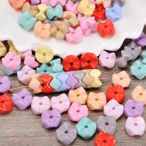 Può includere: Una collezione di perline colorate in plastica di varie forme e dimensioni. Le perline sono in tonalità di rosa, rosso, giallo, blu e grigio. Alcune perline sono a forma di fiore, mentre altre sono rotonde o hanno un design geometrico unico. Ideale per la creazione di gioielli.