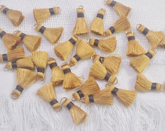 May include: A collection of gold tassel trim with brown accents. The tassels are arranged in a random pattern on a white surface.
