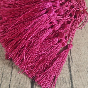 May include: A bunch of bright pink tassels, made of soft, silky fabric. The tassels are tied together and are ready to be used for crafting projects.