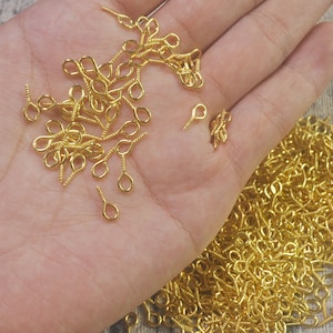 Può includere: Un grande mucchio di fermagli per orecchini a vite dorati. I fermagli sono piccoli e hanno un anello nella parte superiore e un perno a vite nella parte inferiore.