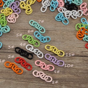 Puede incluir: Una colección de coloridos dijes de cadena en varios tonos, incluyendo naranja, rojo, negro, blanco, verde, azul, amarillo, rosa y morado. Los dijes están esparcidos sobre una superficie de madera.