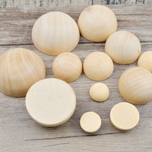 Puede incluir: Una colección de semiesferas y discos circulares de madera sin terminar, de varios tamaños. La veta natural de la madera es visible. Las piezas están dispuestas sobre una superficie de madera marrón claro.