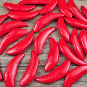 May include: A collection of bright red, glossy, curved, plastic beads. The beads are arranged in a random pattern on a wooden surface.