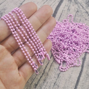 May include: A close-up of a pile of pink metal chains. The chains are made of small, round links and have a shiny finish. The chains are arranged in a loose pile, with some of the chains hanging over the edge of the pile.