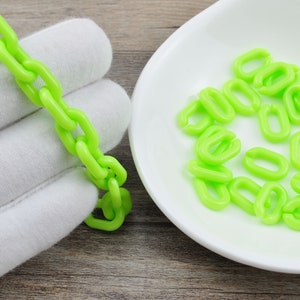 Könnte beinhalten: Nahaufnahme einer leuchtend grünen Plastikkette. Die Kette besteht aus einzelnen ovalen Gliedern. Die Kette liegt auf einer weißen Oberfläche.