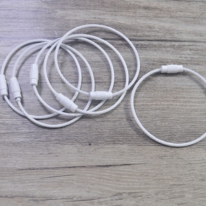 May include: Five white metal key rings with a silver finish. The key rings are linked together and have a small metal loop at the end of each ring.