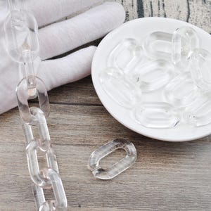 May include: A clear plastic chain with oval links. The chain is lying on a wooden surface. There is a small pile of the same clear plastic oval links in a white dish.