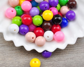 Puede incluir: Un bol lleno de cuentas de plástico de colores en varios tonos de rosa, morado, rojo, verde, amarillo, azul, blanco y marrón. Las cuentas son redondas y lisas, y son perfectas para manualidades o hacer joyas.