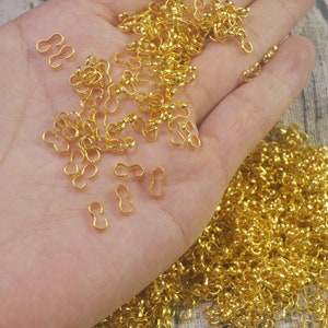 May include: A large pile of gold-colored metal jump rings. The rings are small and have a figure eight shape. They are perfect for jewelry making or other craft projects.