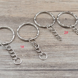 Puede incluir: Cuatro llaveros plateados con cadenas adjuntas. Los llaveros son de diferentes tamaños y las cadenas son de diferentes longitudes. Los llaveros están etiquetados como 1# y 2#.